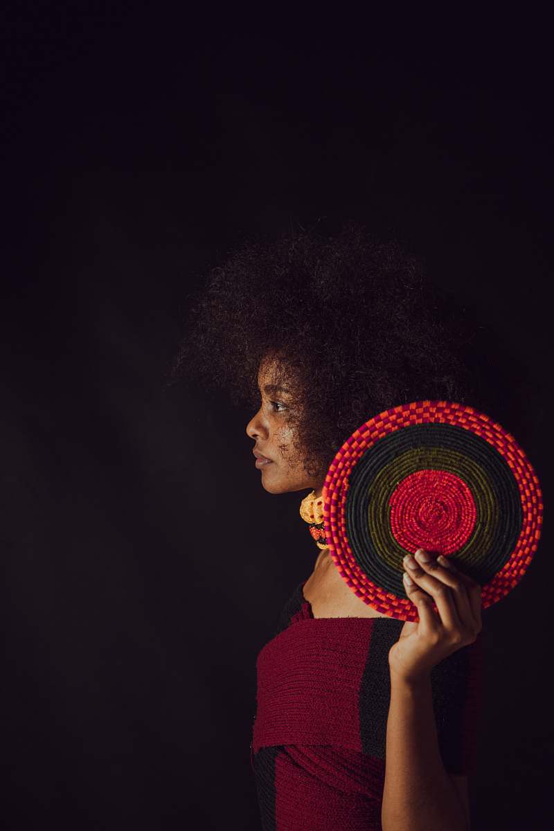 afro hairstyle woman wearing maroon and black top holding round black and red decor human